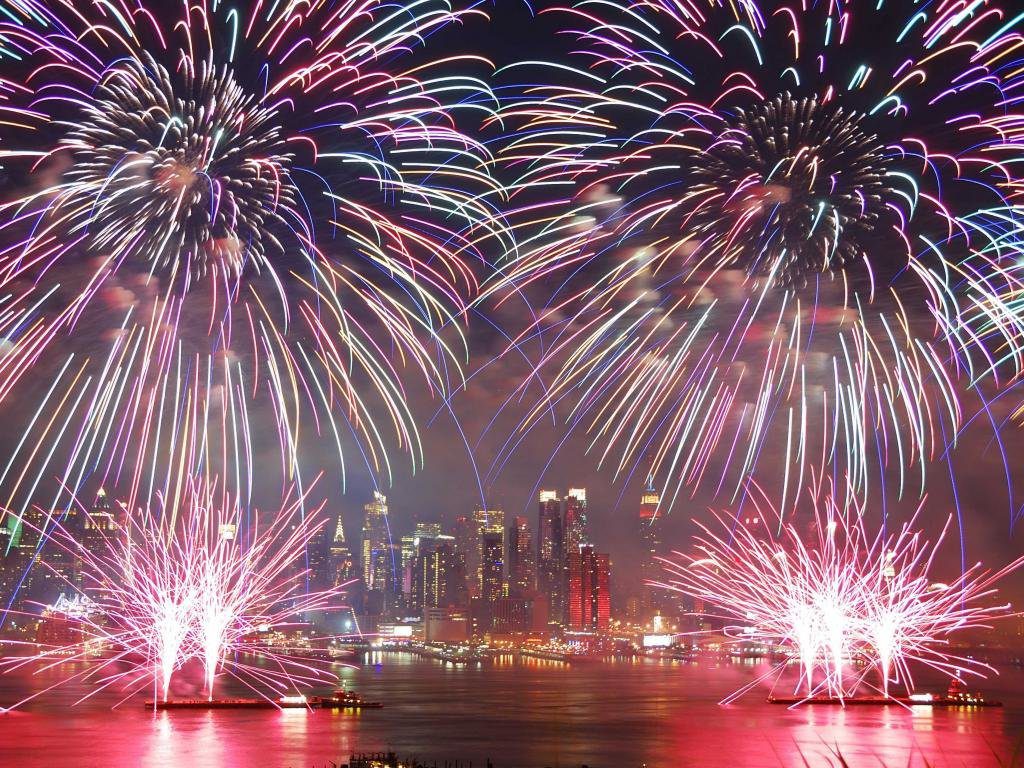 Fireworks over a city at night with the lights on.